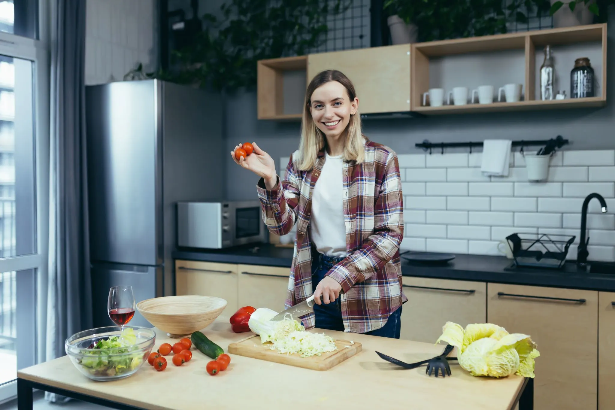 Lena Weber, Autorin von Leckerreise.de, lächelt in die Kamera und hält eine frische Tomate hoch, während sie in der Küche einen Salat zubereitet.