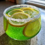 Nahaufnahme eines grünen, prickelnden Alkoholfreie Maibowle Glases mit Zuckerrand und Zitronenscheiben.