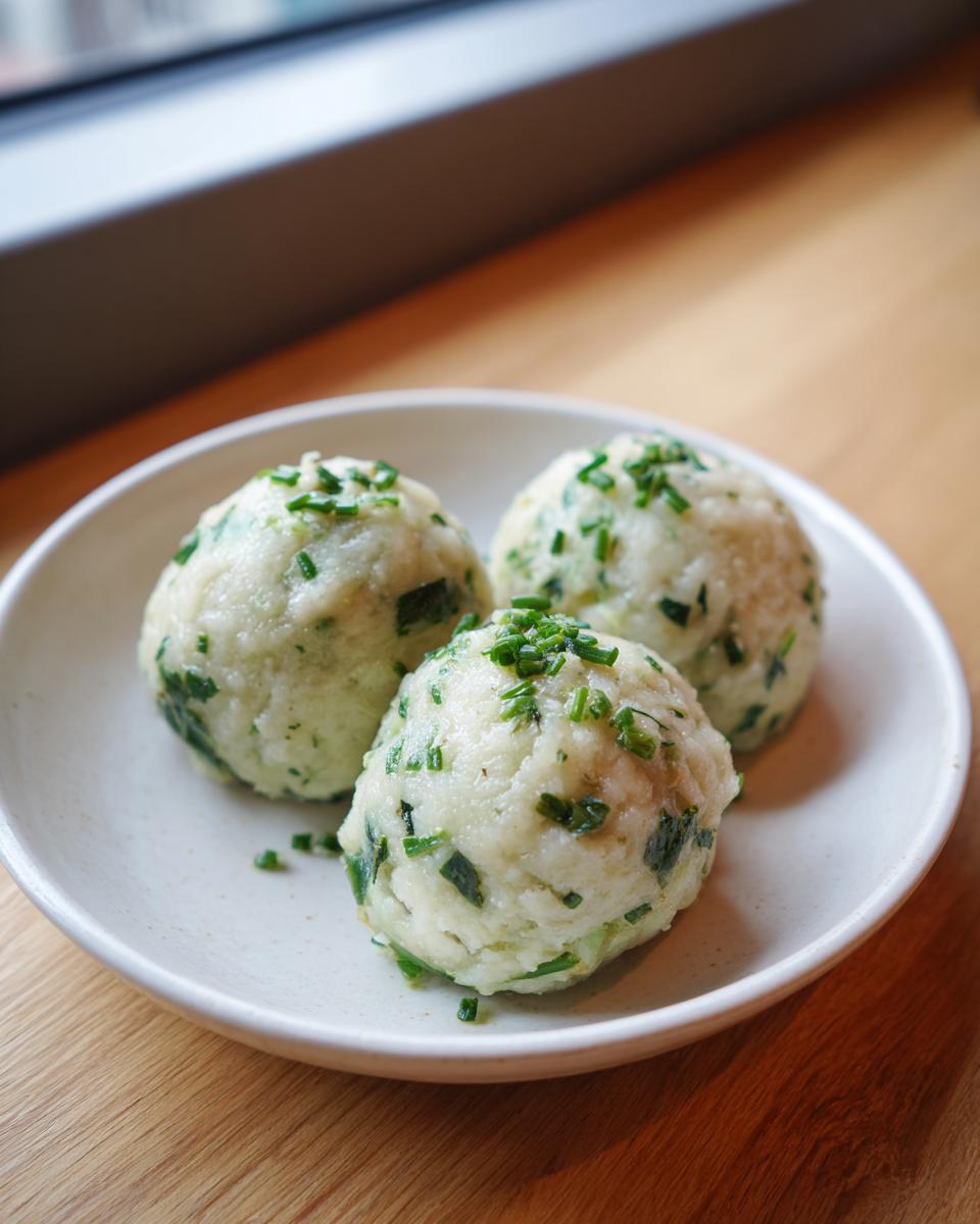 Drei perfekt geformte Bärlauchknödel, garniert mit Schnittlauch, auf einem hellen Teller.