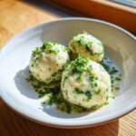 Drei perfekt geformte Bärlauchknödel in einer hellen Schale, übergossen mit zerlassener Kräuterbutter.