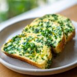 Drei Scheiben Baguette, dick bestrichen mit leuchtend gelber Kräuterbutter und frischen grünen Kräutern.