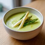 Eine cremige, hellgrüne Spargelcremesuppe garniert mit weißen und grünen Spargelstangen.