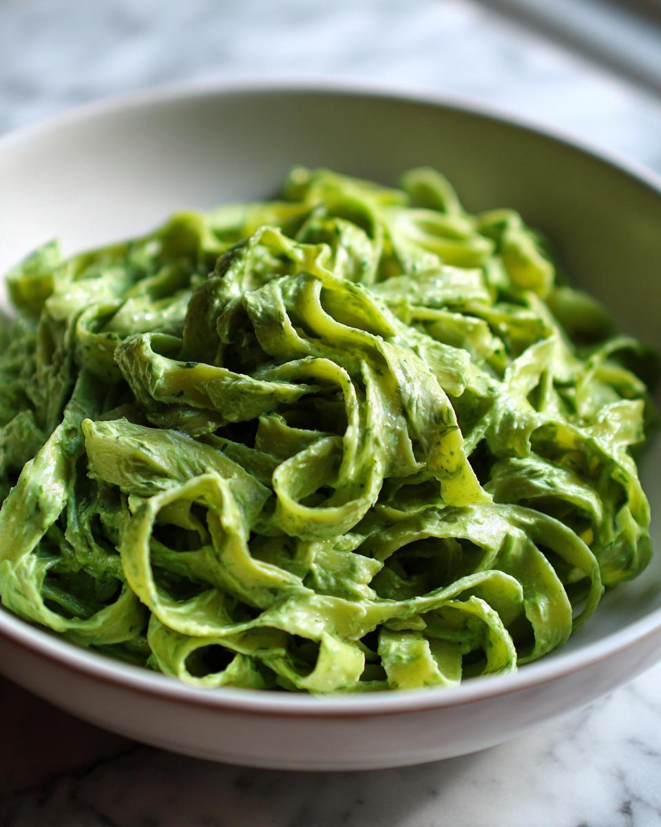 Nahaufnahme von cremigen, grünen Bärlauch Tagliatelle in einer weißen Schüssel.