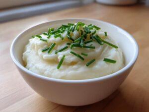 Eine weiße Schüssel mit cremiger Blumenkohlsuppe, garniert mit frischem Schnittlauch.
