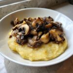 Nahaufnahme von cremiger Polenta mit Pilzen, die in einer weißen Schüssel angerichtet sind.