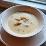 Nahaufnahme einer cremigen, hellen Spargelsuppe in einer weißen Schüssel mit sichtbaren Spargelstücken.