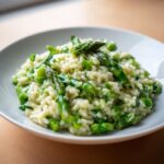 Nahaufnahme von cremigem Spargel-Risotto mit grünen Spargelstücken in einer weißen Schale.