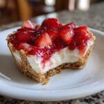 Nahaufnahme eines angeschnittenen Erdbeer-Joghurt-Törtchen mit Keksboden und cremiger Füllung.