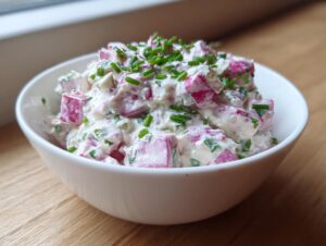 Nahaufnahme von cremigem Radieschen-Dip mit rosa Radieschenstücken und Schnittlauch in einer weißen Schale.