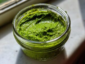 Nahaufnahme von leuchtend grüner veganer Bärlauchpaste in einem kleinen Glas.
