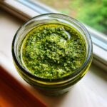 Nahaufnahme von leuchtend grünem Bärlauch-Pesto in einem Glas, bedeckt mit einer Schicht Öl.