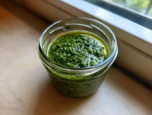 Nahaufnahme von selbstgemachtem Bärlauch-Pesto in einem kleinen Glas, bedeckt mit einer Ölschicht.