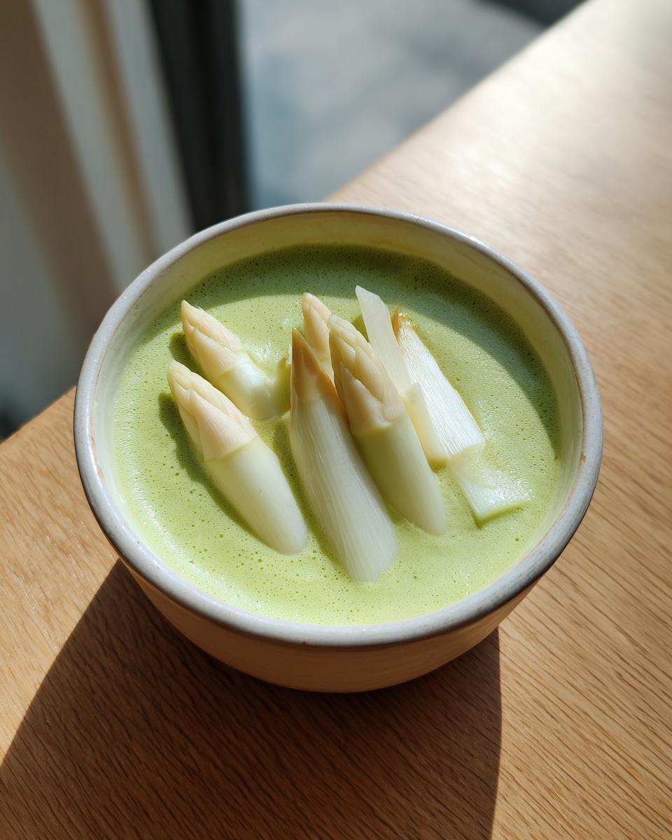 Nahaufnahme einer grünen Spargelcremesuppe, garniert mit ganzen weißen Spargelspitzen.