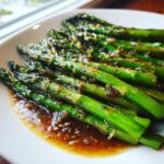 Gedämpfter grüner Spargel übergossen mit brauner Nussbutter auf einem weißen Teller.