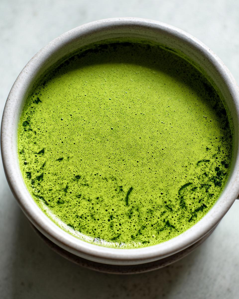 Nahaufnahme einer Tasse mit leuchtend grüner, schaumiger Bärlauchsuppe, die eine intensive Farbe zeigt.