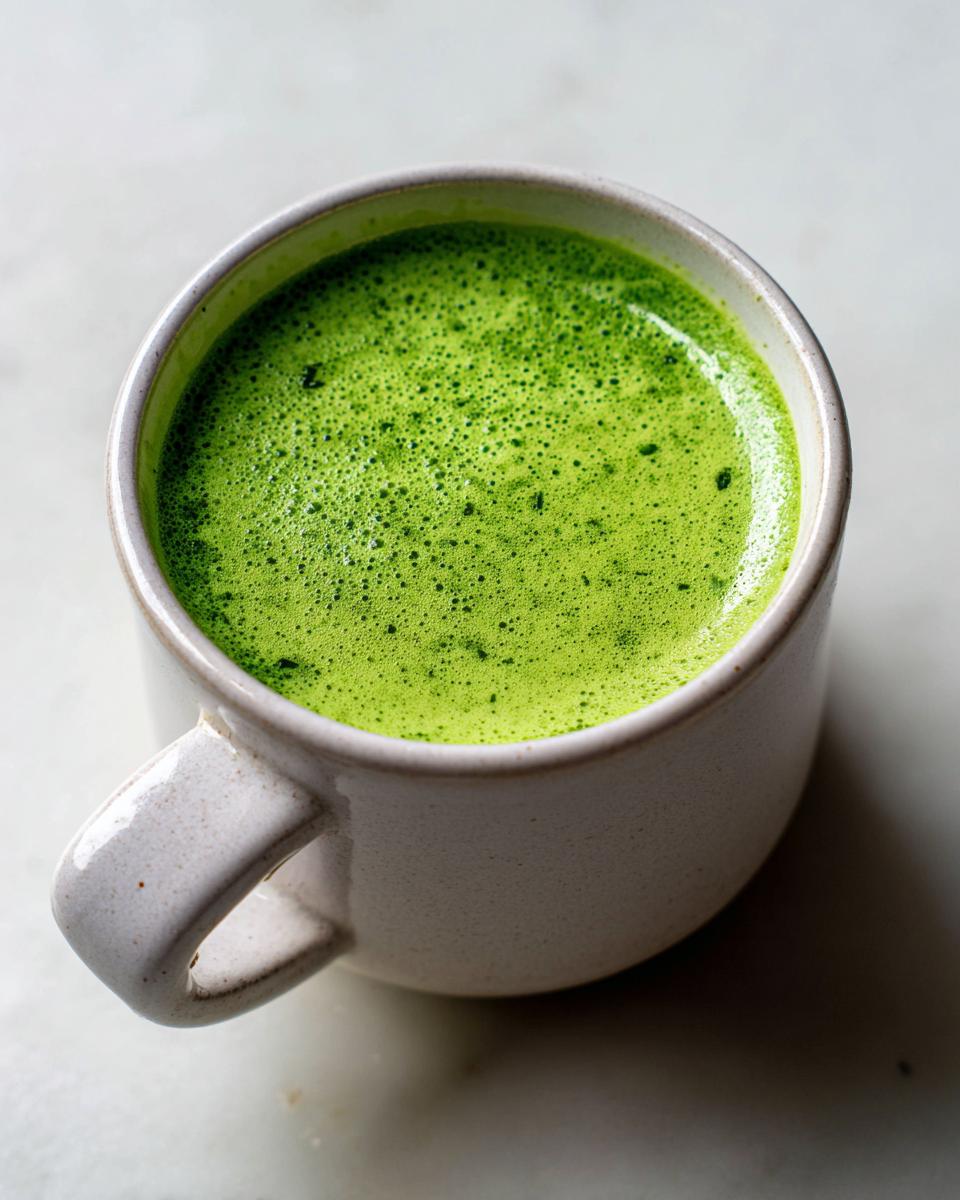 Nahaufnahme einer Tasse mit leuchtend grüner, schaumiger Bärlauchsuppe auf hellem Untergrund.