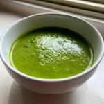 Nahaufnahme einer leuchtend grünen Bärlauchsuppe in einer weißen Schüssel, die die intensive Farbe hervorhebt.