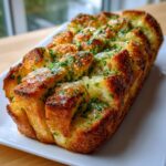 Ein goldbraun gebackenes, saftiges Kräuter-Zupfbrot, bestreut mit Petersilie, auf einem weißen Servierteller.