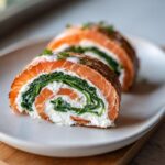 Zwei Scheiben einer aufgeschnittenen Lachsrolle zum Muttertag mit einer Füllung aus grünem Spinat und weißem Frischkäse auf einem weißen Teller.