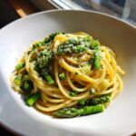 Nahaufnahme von Pasta mit grünem Spargel, bestreut mit geriebenem Parmesan.