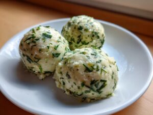 Drei perfekt geformte Bärlauchknödel mit viel grünem Bärlauch auf einem weißen Teller.
