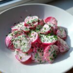 Nahaufnahme eines cremigen Radieschensalat mit Schnittlauch in einer weißen Schüssel.