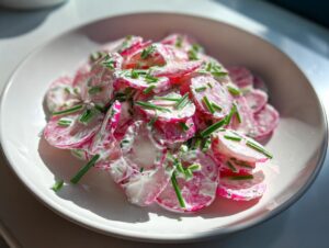 Nahaufnahme von cremigem Radieschensalat mit geschnittenen Radieschen und frischem Schnittlauch auf einem weißen Teller.