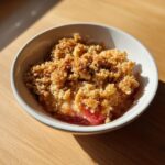 Nahaufnahme eines Rhabarber Crumble in einer weißen Schale mit goldbraunen, knusprigen Streuseln.