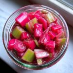 Nahaufnahme von leuchtend rotem und grünem Rhabarberkompott, das in einem Glas konserviert wird.