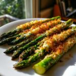 Nahaufnahme von grünem Spargel mit goldbrauner, knuspriger Spargel mit Parmesankruste auf einem weißen Teller.