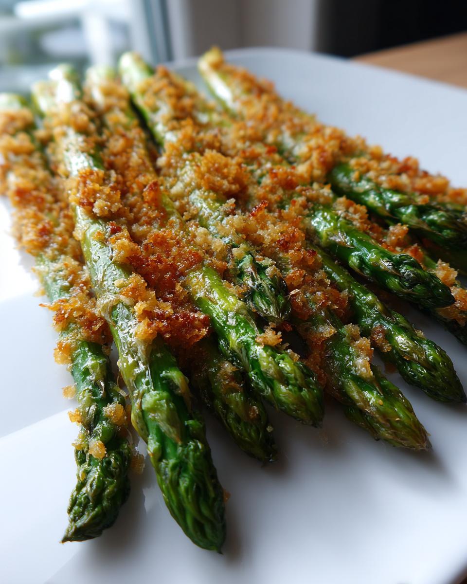 Nahaufnahme von grünem Spargel mit einer goldbraunen, knusprigen Parmesankruste auf einem weißen Teller.
