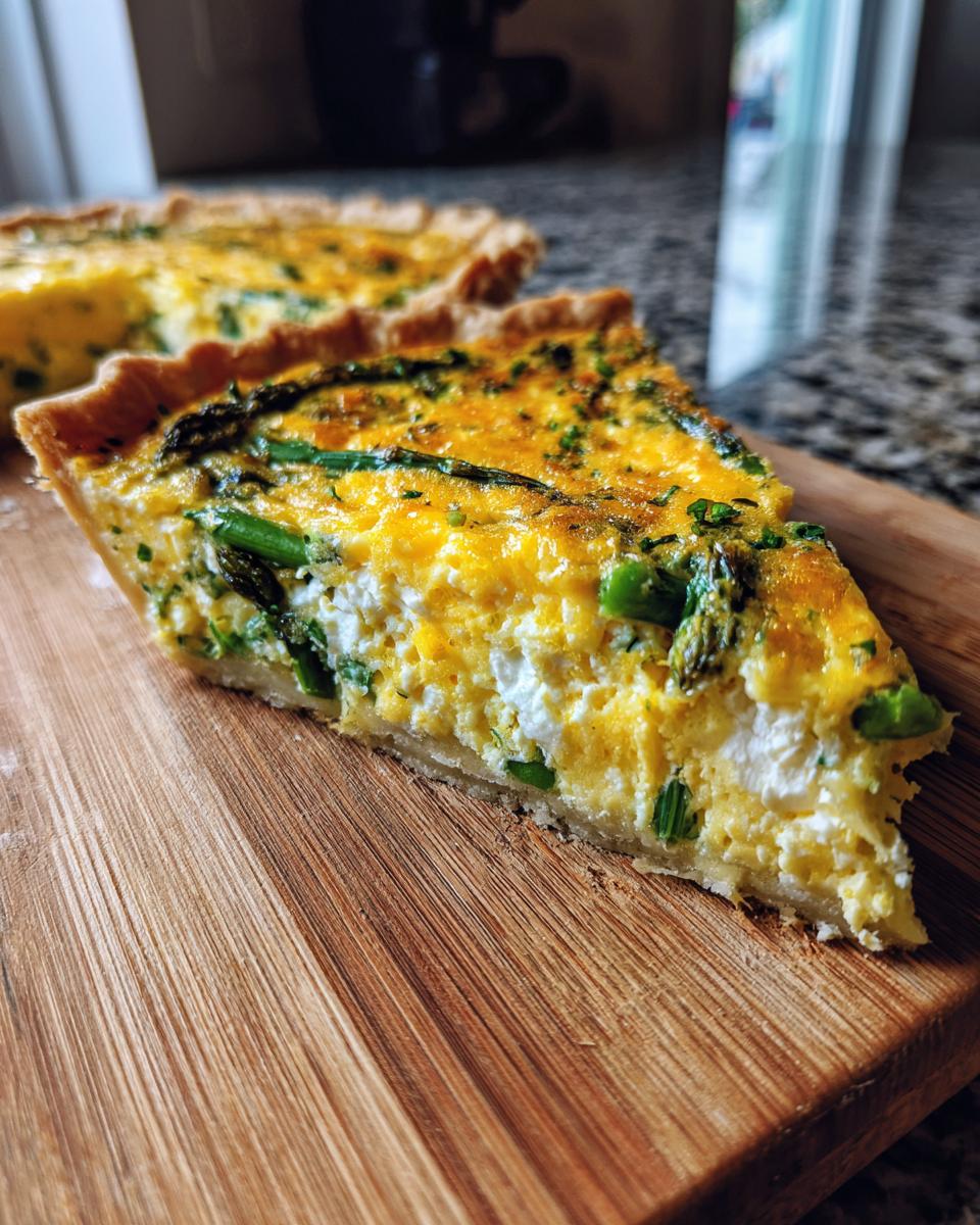 Ein angeschnittenes Stück cremiger Spargelquiche mit grünem Spargel und Kräutern auf einem Holzbrett.