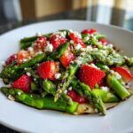 Nahaufnahme eines Spargelsalat mit Erdbeeren, zerbröseltem Feta und Balsamico-Dressing auf einem weißen Teller.