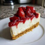 Ein cremiges Stück Erdbeer-Käsekuchen mit Keksboden und glänzendem Erdbeer-Topping auf einem weißen Teller.