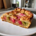 Nahaufnahme eines Stücks Rhabarber Galette mit aufrecht stehenden, roten und grünen Rhabarberstücken auf einem weißen Teller.