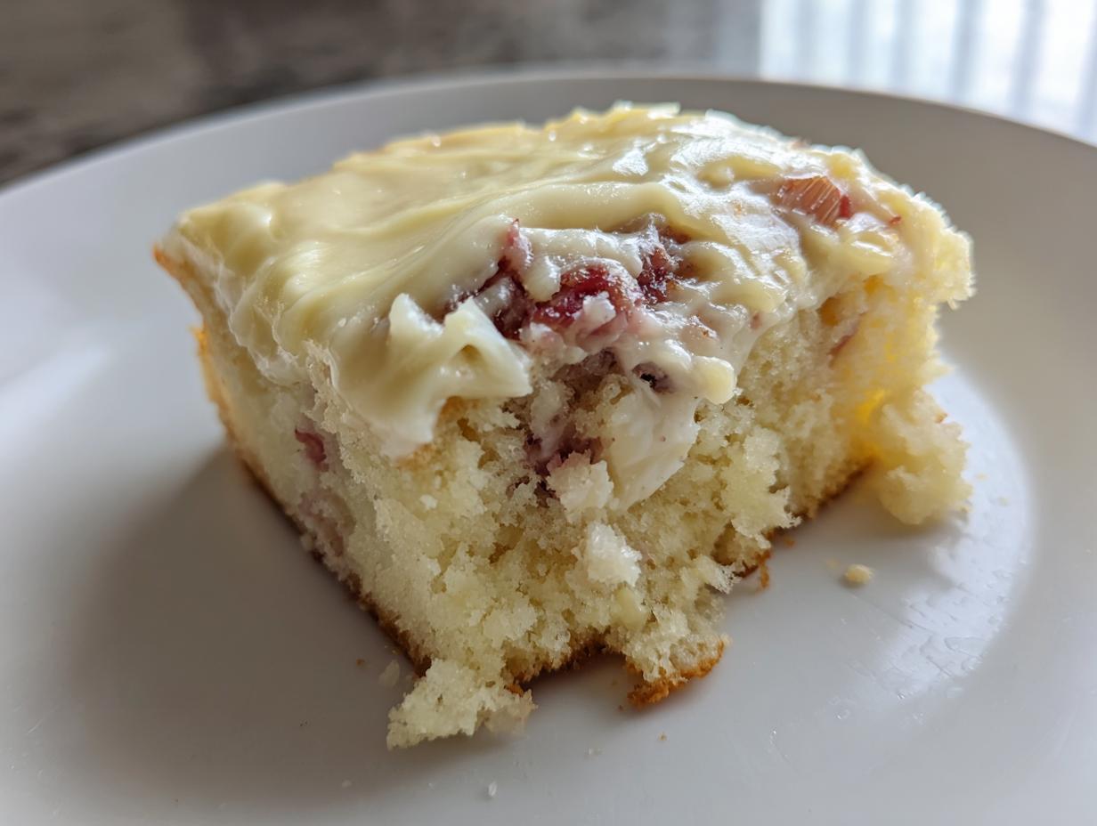 Nahaufnahme eines Stücks Rhabarber-Schmandkuchen mit saftigem Boden und dicker Schmanddecke.
