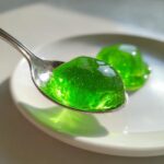 Nahaufnahme von leuchtend grünem Waldmeister-Gelee, das auf einem silbernen Löffel gehalten wird.