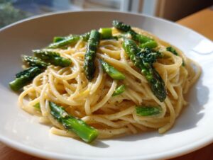 Nahaufnahme einer cremigen Zitronenpasta mit grünem Spargel in einem weißen Teller.