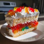 Ein Stück saftige Gummibärchen-Torte mit Biskuitboden, bunter Götterspeise und Sahnehaube.