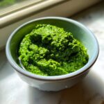 Nahaufnahme von leuchtend grünem Bärlauchpesto selber machen in einer kleinen blauen Schale.