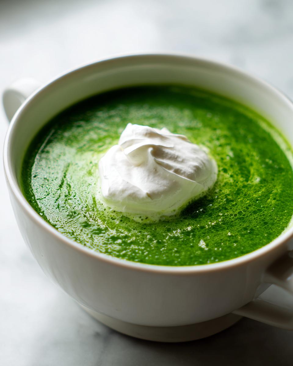 Nahaufnahme einer leuchtend grünen Bärlauchschaumsuppe, garniert mit einem Klecks weißer Schlagsahne in einer weißen Tasse.