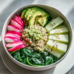 Nahaufnahme einer Bunte Gemüse-Bowl mit Quinoa, Avocado, Radieschen, Gurke und Spinat.