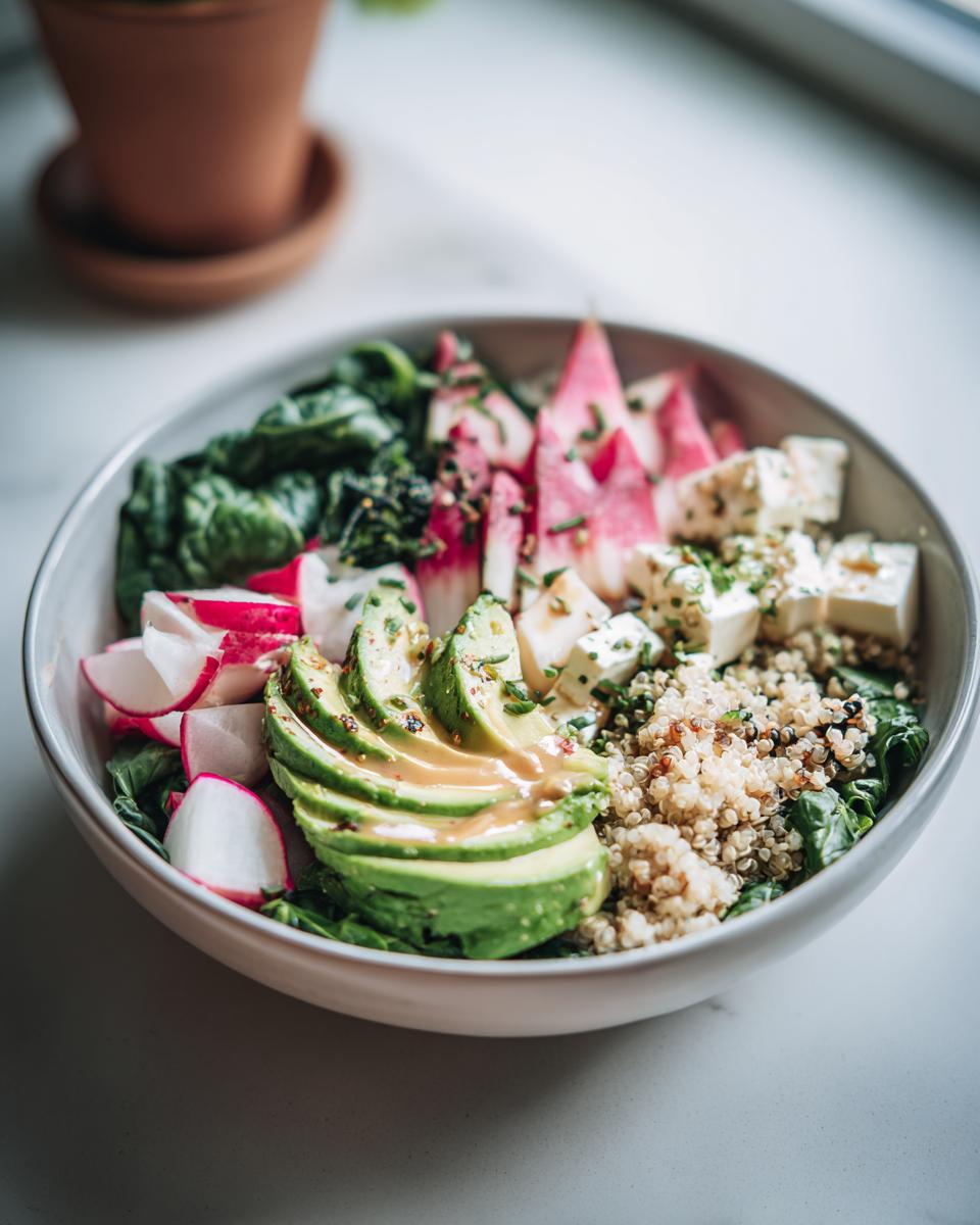 Nahaufnahme einer Bunte Gemüse-Bowl mit geschnittenen Avocadoscheiben, Radieschen, Feta und Quinoa.