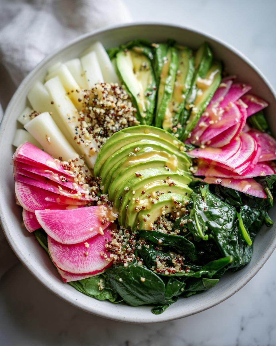 Nahaufnahme einer Bunte Gemüse-Bowl mit Scheiben von Avocado, rosa Rettich, weißem Gemüse und Quinoa.