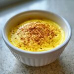Nahaufnahme einer cremigen, gelben Sauce Hollandaise in einer weißen Schale, bestreut mit frisch geriebener Muskatnuss.