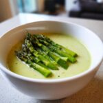 Nahaufnahme einer cremigen, hellgrünen Spargelsuppe, garniert mit gegrillten grünen Spargelstangen.