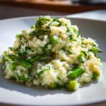Nahaufnahme von cremigem Spargel-Risotto mit grünen Spargelstücken auf einem weißen Teller.