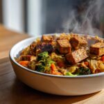 Nahaufnahme einer dampfenden Sauerkraut-Pfanne mit gebratenem Tofu, Brokkoli und Karotten in einer weißen Schüssel.