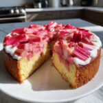 Angeschnittener Einfacher Rhabarberkuchen mit Schmand, belegt mit leuchtend roten Rhabarberstücken.
