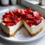 Ein Anschnitt des cremigen Erdbeer-Käsekuchen ohne Backen mit einem Keksboden und frischen Erdbeeren obenauf.